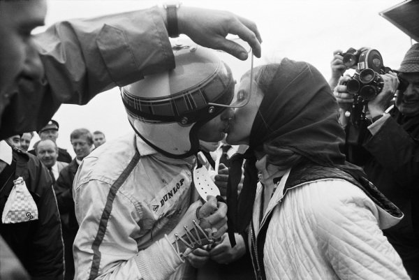 Helen Stewart kisses her husband, Jackie, after his win. Somebody is helpfully holding Jackie's visor up as his broken wrist is in a cast. Helen Stewart kisses her husband, Jackie, after his win. Somebody is helpfully holding Jackie's visor up as his broken wrist is in a cast.